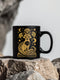 A black ceramic mug featuring a stylized golden fox design surrounded by Art Deco ginkgo fans, crescent moons, and stars. The mug has a glossy finish and ergonomic handle.